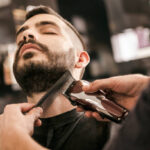 Man getting his beard trimmed with electric razor at hairdesser